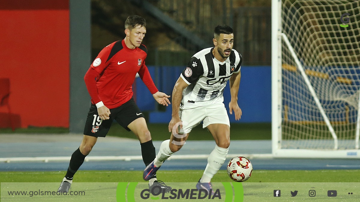 Joe Winstanley en un partido del CF La Nucía, compitiendo con un balón con Carles Síscar. 