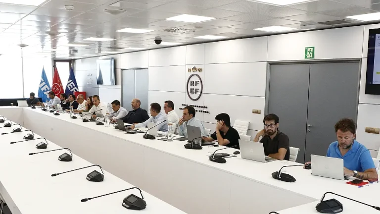 Reunión de la RFEF con representantes de clubes de la Primera Federación, con pantallas y laptops en una sala moderna.